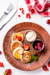 Cottage cheese pancakes, homemade traditional Ukrainian dish syrniki with berry sauce and sour cream on a brown plate on a white background, vertical photo