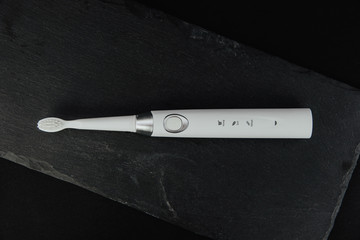 White sonic toothbrush on a dark stone background. Medical and dental concept. Caring for teeth, modern methods of removing calculus from teeth. Electric toothbrush.