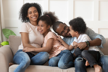 Happy african american family of four laughing bonding on sofa