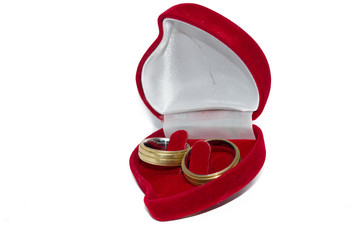 small red heart shaped jewelry holder box and a pair of golden wedding rings, isolated on white background