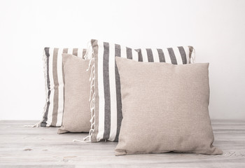 Striped and gray cushions on the wooden table side view. Soft square pillows on a wooden surface...