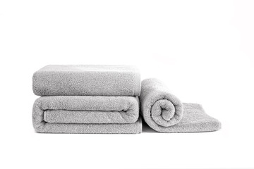 Three gray terry towels rolled, folded and stacked isolated. Terry towels against white backdrop. Folded and rolled soft bath towels. Stack of grey cotton towels on a white background