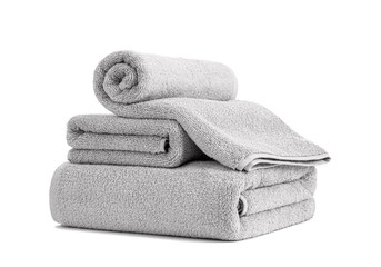 Gray terry towels rolled, folded and stacked isolated. Stack of terry towels against white backdrop. Folded and rolled soft bath towels. Stack of three grey cotton towels on a white background.