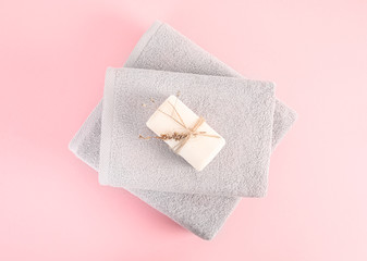 Two folded and stacked terry towels with soap and dry herbs steam on the pink background. Stack of gray clean towels isolated. Top view.