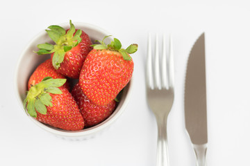 Fresh strawberry, fork and knife. White background.