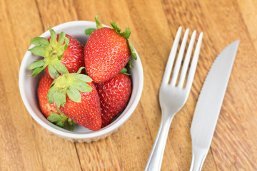 Fresh strawberry, fork and knife. Wooden background.