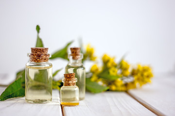 Transparent bottle with cork stopper with yellow oil on a background of wildflowers