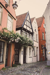 Bremen, Germany - 06/13/2019: street in old town of Bremen with floral decoration. Medieval buildings with roses on wall. Ancient architecture in Europe. Facade design with flowers. Ornamental plants.