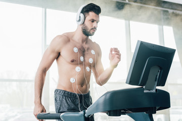 muscular sportsman in headphones running on treadmill during endurance test in sports center