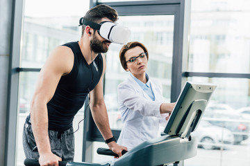 sportsman in vr headset training on treadmill near doctor during endurance test in gym