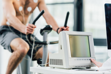 Fototapeta na wymiar Cropped view of sportsman with electrodes training on elliptical during endurance test in gym