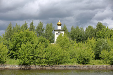 The golden dome of the white stone Orthodox church on the bank of the river