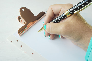 Female hand writes with a ballpoint pen on a clean sheet of paper on a clipboard..