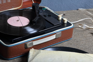 An old gramophone with a vinyl record mounted on it. Next to shabby paper envelopes are other records.