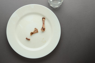 Plate white empty dusty ceramic round with bare bones and a dirty glass on a gray background with shadows.