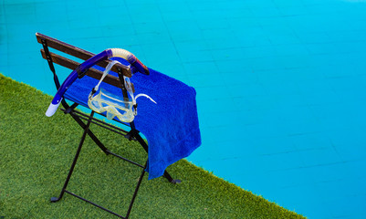 water sport and activities concept picture of wooden chair with blue towel and snorkeling mask and tube equipment on a green grass floor near swimming poll background texture empty space for copy 