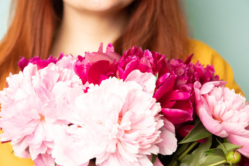 Happy girl with a bouquet of peonies on light blue background