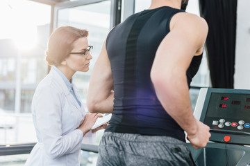 sportsman training on treadmill near doctor during endurance test in gym