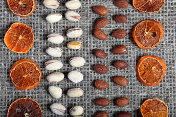 Dried orange slices, pistachios and almonds are laid out in rows on coarse linen fabric.