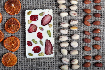 Dried orange slices, pistachios and almonds are lined up in rough linen fabric. White chocolate decorated with dried fruit.