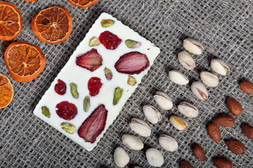 Dried orange slices, pistachios and almonds are lined up in rough linen fabric. White chocolate decorated with dried fruit.