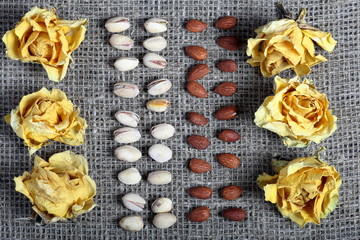 Pistachios and almonds are laid out in rows on coarse linen fabric. Decorated with dried flowers of yellow roses.