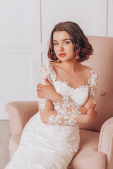 Fototapeta na wymiar Young beautiful bride in a lace wedding dress is sitting in a pink chair
