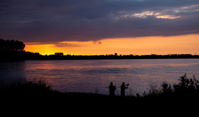 Fototapeta premium fischer fischen aus eine Flussufer bei Sonnenuntergang mit schönes Warmes Licht