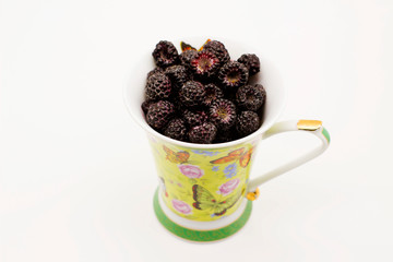 black raspberries in a mug on a white background