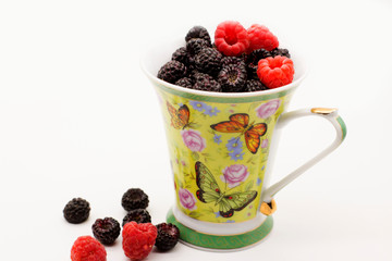 black and red raspberries in a mug on a white background
