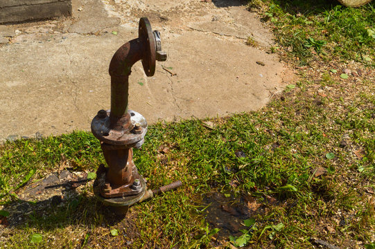 An iron rusty corrosive old industrial water supply pipe for water supply with a flange moving with nuts and studs sticks out of the ground of green grass