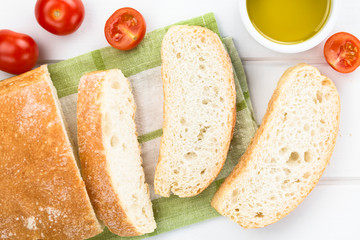 Fresh Italian ciabatta bread sliced, cherry tomatoes and olive oil on the side, photographed overhead on white wood (Selective Focus, Focus on the bread slices)
