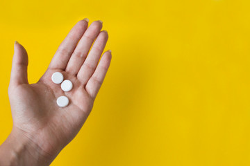 white round pills in female hand on yellow background with copy space