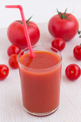 A glass of tomato juice and red tomatoes on a white background