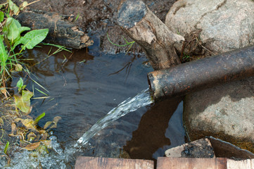 Source of water on the bank of the river - clear water pours from a pipe against the background of earth and grass