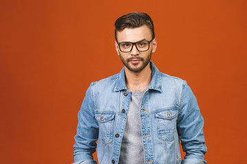 Fototapeta premium Casually handsome. Confident young handsome man in jeans shirt smiling while standing against orange background.
