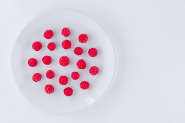 Raspberries on a white plate. Red raspberry berries on a white background. Berries for vegan. Summer concept. Minimalistic food. Top view. Copy space