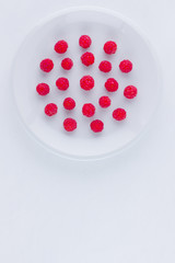 Raspberries on a white plate. Red raspberry berries on a white background. Berries for vegan. Summer concept. Minimalistic food. Top view. Copy space