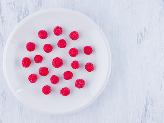 Raspberries on a white plate. Red raspberry berries on a white background. Berries for vegan. Summer concept. Minimalistic food. Top view. Copy space