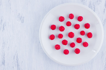Raspberries on a white plate. Red raspberry berries on a white background. Berries for vegan. Summer concept. Minimalistic food. Top view. Copy space