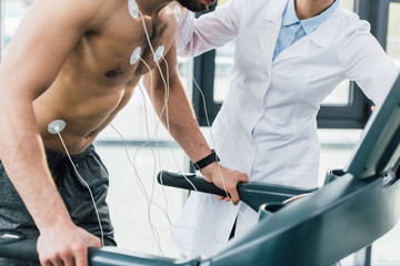 cropped view of doctor putting electrodes on shirtless sportsman during endurance test