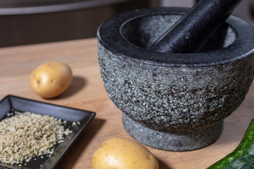 Mortar and pestle made of stone on a kitchen counter with potatoe, hemp seeds and cucumber