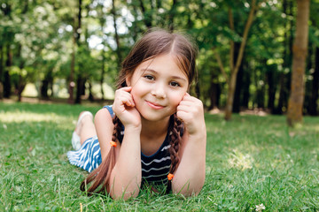 Cute little girl laying on green fresh grass outdoor