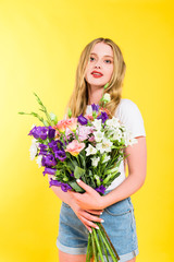 attractive blonde girl with flowers looking at camera On yellow