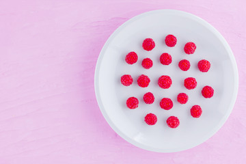 Raspberries on a white plate. Red raspberry berries on a pink background. Berries for vegan. Summer concept. Minimalist food. Top view. Copy space