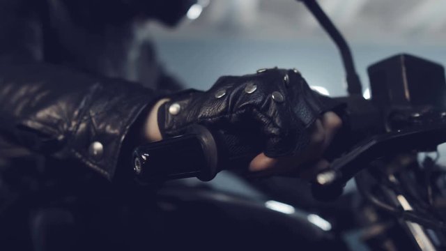 Brutal biker girl sits on a black motorcycle and turns the speed knob. Preparing for night races. Moto service. Frame for the film.