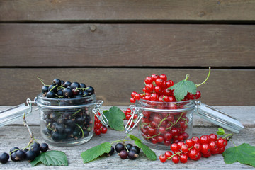 Jars filled with black and red currant on the background of brown planks