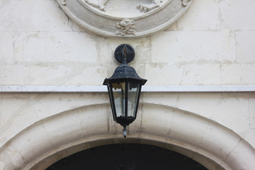 Fototapeta na wymiar Old forged lantern on house facade. Street view of lamp light on building front, close up 
