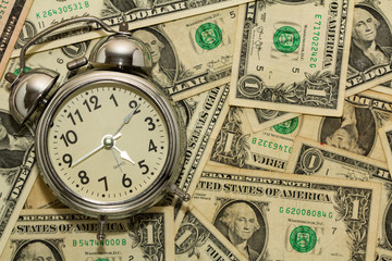 Alarm clock on carpet of dollar bills, time is money.