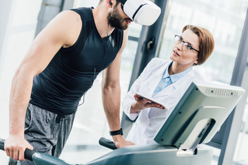 sportsman in vr headset training on treadmill near doctor during endurance test in gym
